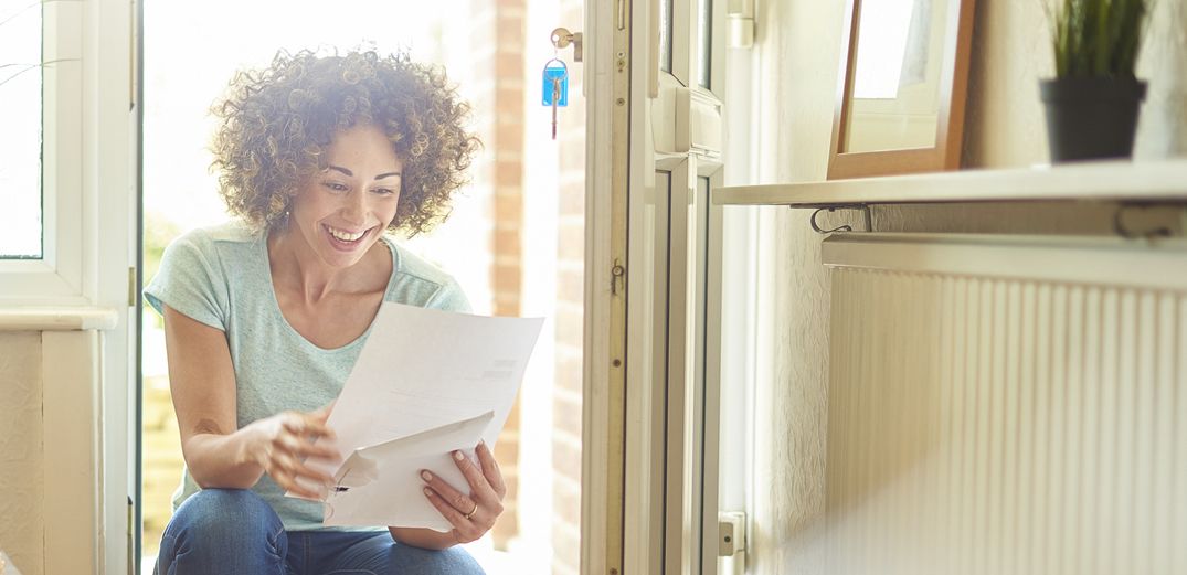 A happy woman reviews her paper Roth IRA statement in sun-filled room.