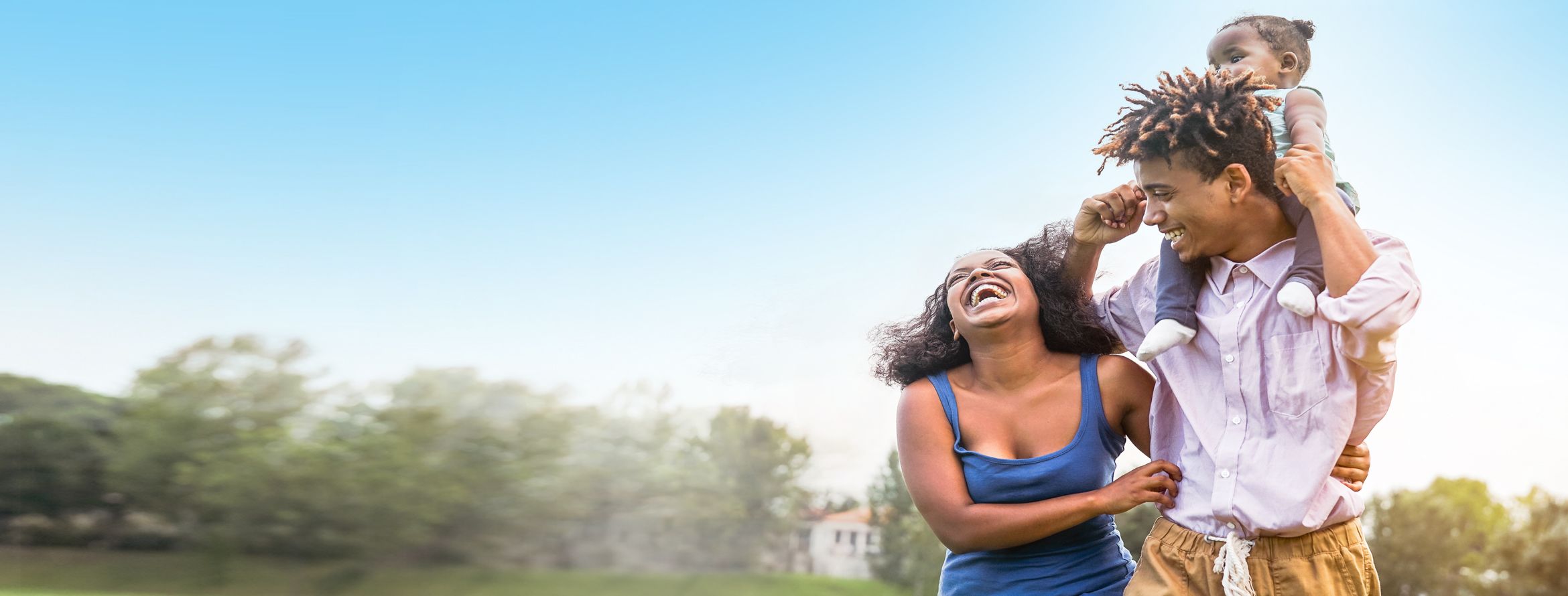 A happy and laughing family outside enjoying each other's company with the daughter on the fathers shoulders