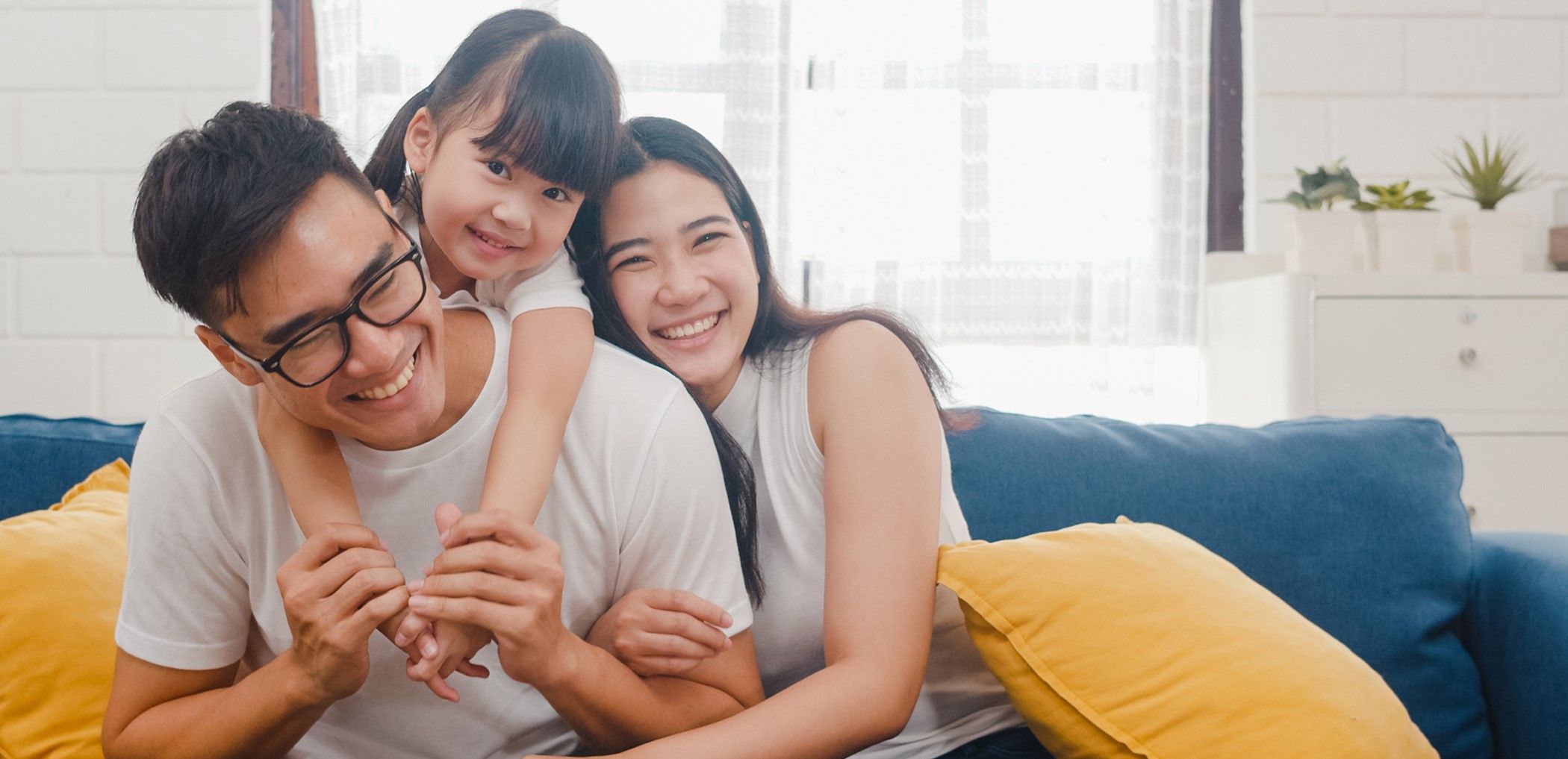 A little girl climbs up onto her young dad's back as mom smiles.