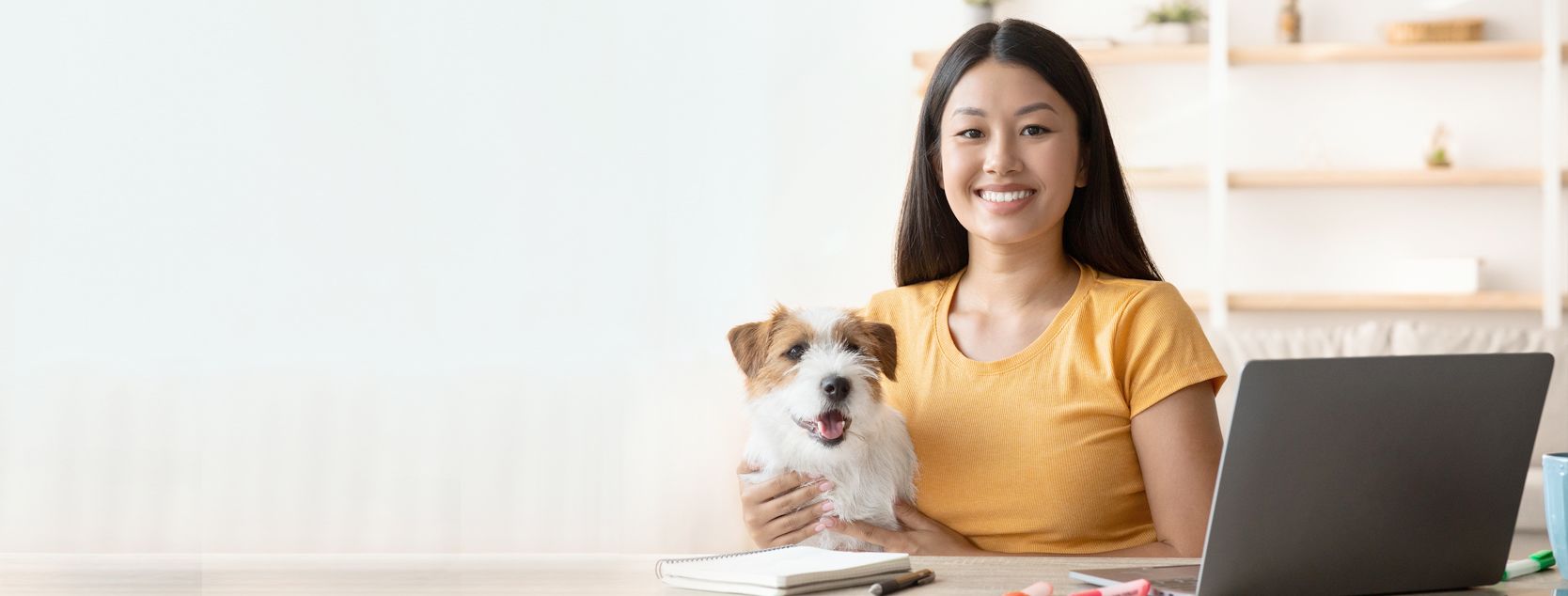 A smiling woman with her dog in her lap signs into Patelco Online from her home laptop.